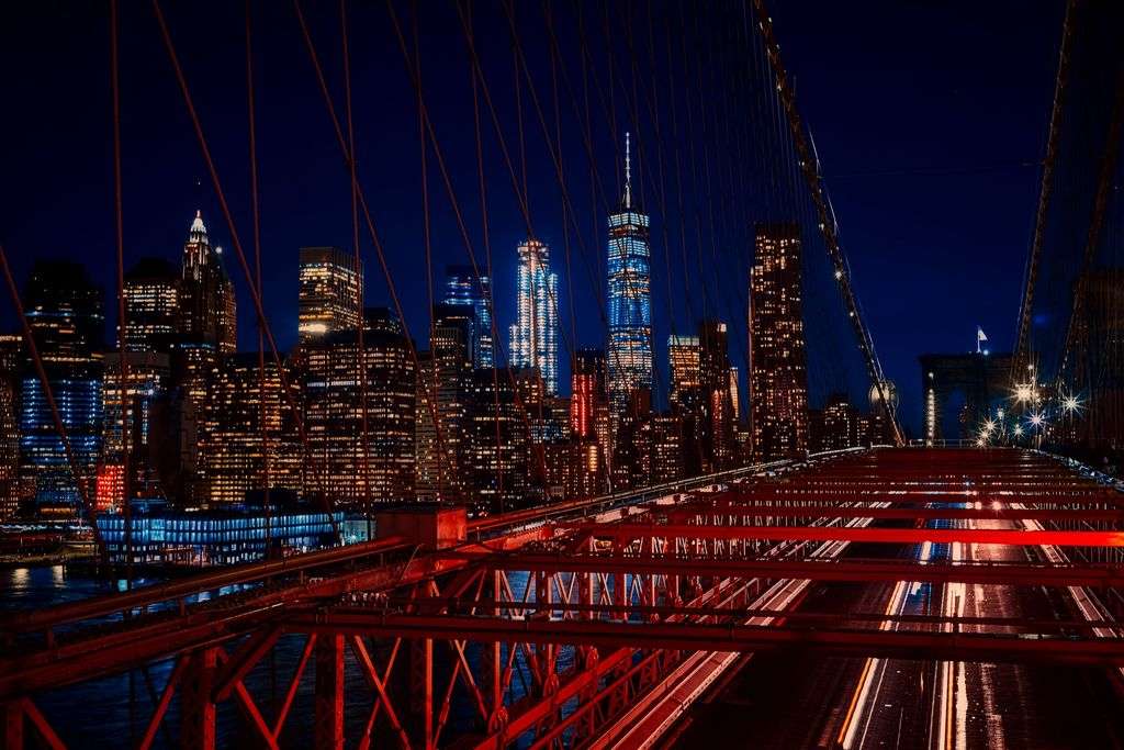 A breathtaking night view featuring the New York City skyline and iconic Brooklyn Bridge illuminated in vibrant colors.